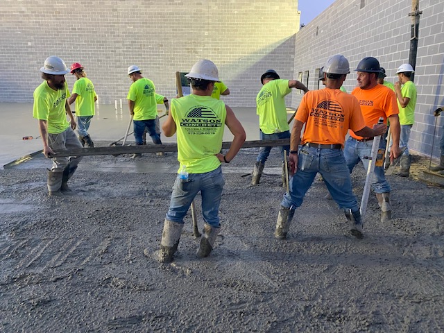 Watson Concrete employees stand in wet concrete on a job site.