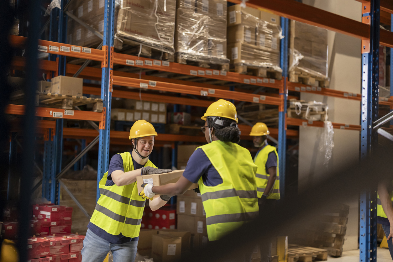 Warehouse workers with disabilities collaborating to move boxes, highlighting inclusion and teamwork.