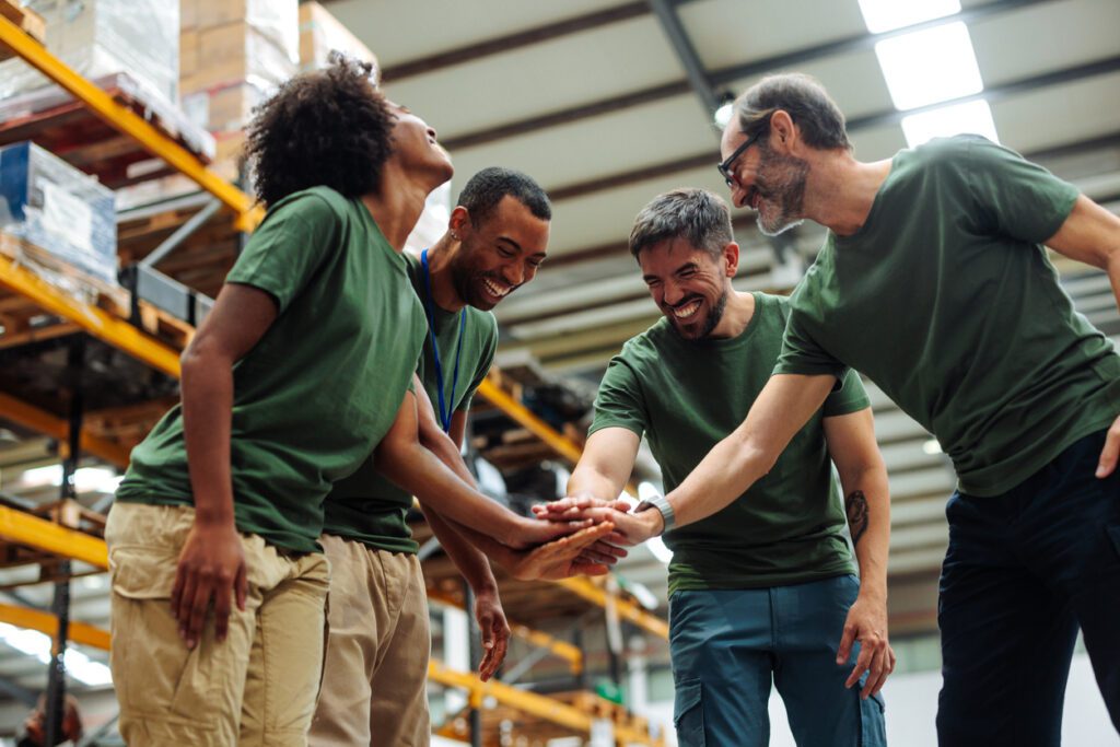 Happy warehouse workers joining hands together, celebrating success and showing strong teamwork in a distribution center