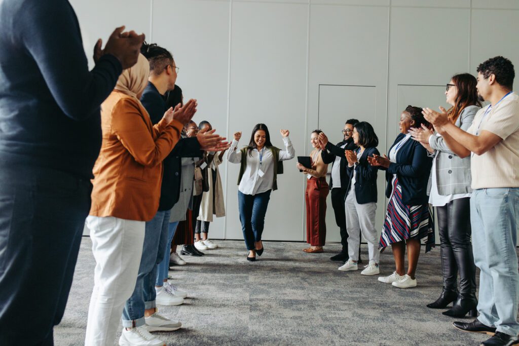 A diverse group of business professionals applauding and celebrating a woman in a corporate setting, reflecting teamwork, achievement, and inclusivity.