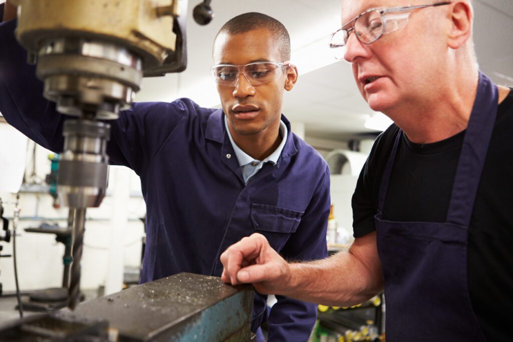Engineer Teaching Apprentice To Use Milling Machine At Work