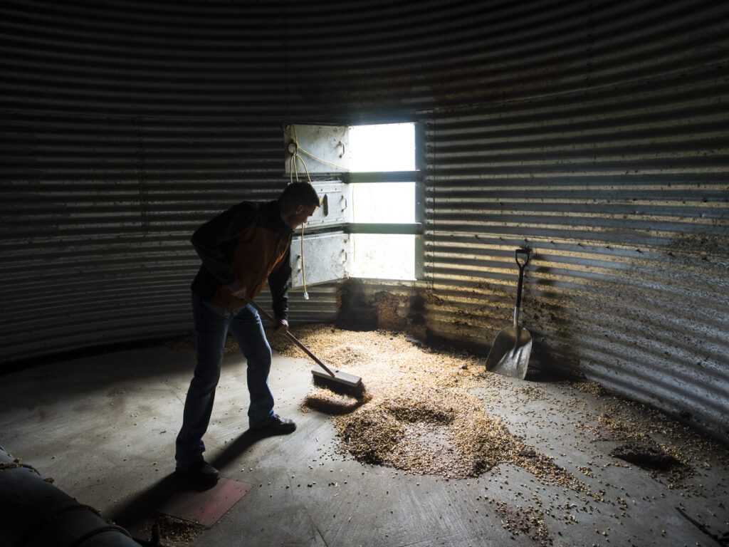 Man cleaning residual corn out of a grain storage bin